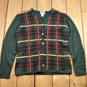 May include: A green cardigan with a plaid pattern in red, yellow, and black. The cardigan has a v-neck and button closure.