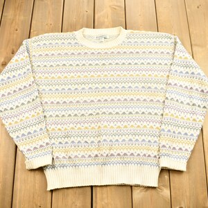 Puede incluir: Un suéter de color crema con un patrón geométrico colorido. El patrón presenta rayas azules, amarillas y rosas.