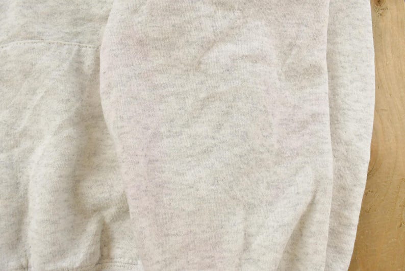 Op de afbeelding: Een lichtgrijs gem&ecirc;leerd sweatshirt met een zachte, fleeceachtige textuur over de gehele stof. Het kledingstuk vertoont een consistent gespikkeld patroon met donkerdere grijze vezels geweven in het lichtgrijze basismateriaal voor een klassieke uitstraling.