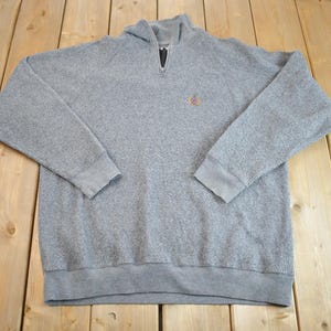 May include: A grey, long-sleeved sweatshirt with a zipped neck and a small embroidered logo on the chest.