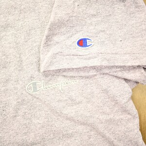 May include: A heather grey t-shirt with a white Champion logo on the right sleeve and a white Champion logo on the front of the shirt.