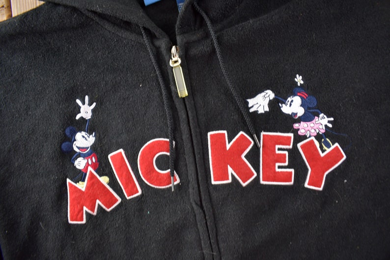 May include: Black hooded sweatshirt with a red embroidered Mickey Mouse design. The design features Mickey Mouse and Minnie Mouse with the word "MICKEY" in red.