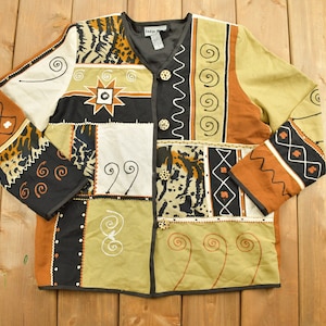 Puede incluir: Una chaqueta multicolor con un diseño de patchwork que presenta estampado animal, patrones geométricos y remolinos. La chaqueta tiene cierre de botón y mangas largas.