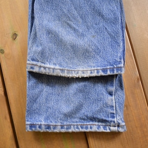 May include: A pair of blue denim jeans folded in half, showing the hem of the jeans. The jeans have a faded look and a frayed hem.