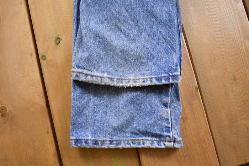 May include: A pair of blue denim jeans folded in half, showing the hem of the jeans. The jeans have a faded look and a frayed hem.