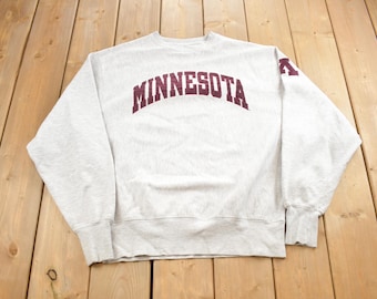 May include: A gray sweatshirt with a maroon "MINNESOTA" arch across the front. The sweatshirt has maroon accents on the sleeves.