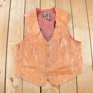 May include: A brown leather vest with a button closure and two pockets. The vest has a red lining and a label that says "CERVO" with a deer head logo.