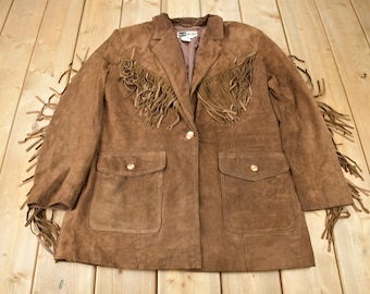 May include: Brown suede jacket with fringe detailing on the collar, pockets, and sleeves. The jacket has a single button closure and two flap pockets.