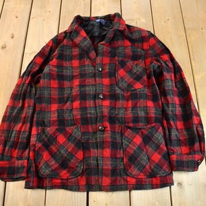 May include: A red and black plaid flannel shirt with two large pockets on the front. The shirt has a button-up front and a collar.