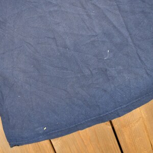 May include: A dark blue t-shirt with a smooth, slightly textured surface. The t-shirt is folded and lying on a wooden surface.