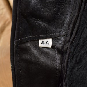 May include: Close-up of a black leather garment with a white size tag that reads "44".