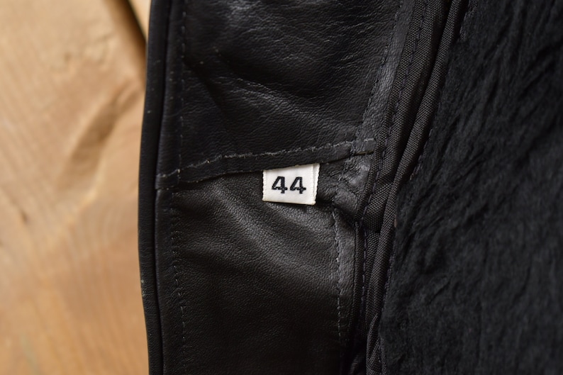 May include: Close-up of a black leather garment with a white size tag that reads "44".