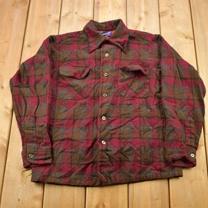 May include: A red and brown plaid flannel shirt with long sleeves and a button-up front.