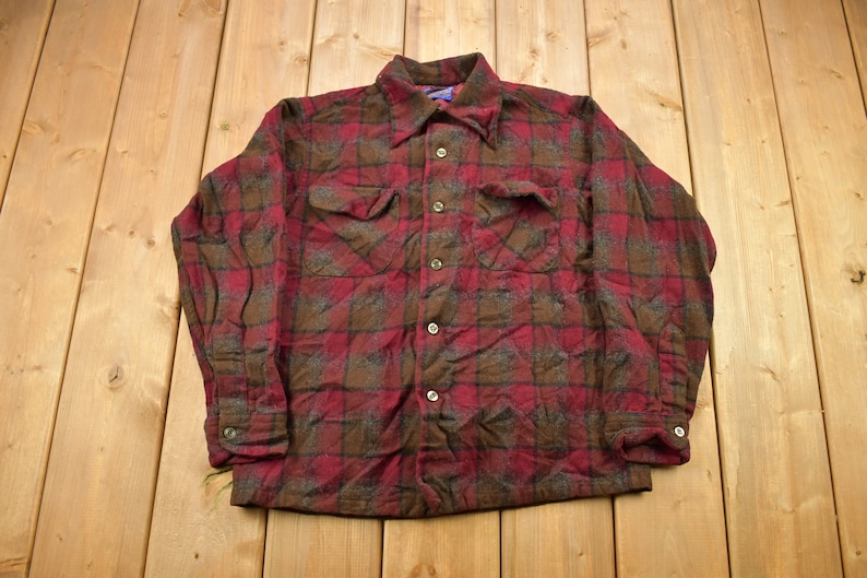 May include: A red and brown plaid flannel shirt with long sleeves and a button-up front.