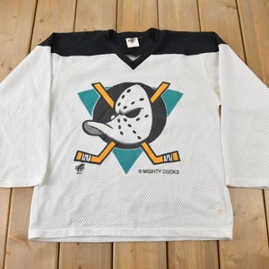 May include: White hockey jersey with a black and teal Mighty Ducks logo featuring a cartoon duck wearing a goalie mask. The jersey has a mesh fabric and long sleeves.