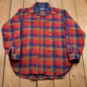 May include: A red, blue, and brown plaid flannel shirt with long sleeves and a button-up front.