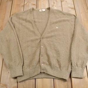 Peut inclure: Un cardigan en laine marron avec un devant boutonné et un petit logo sur la poitrine gauche.
