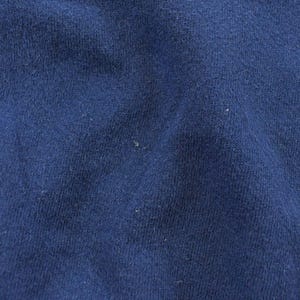 K&ouml;nnte beinhalten: Nahaufnahme eines strukturierten, marineblauen Stoffes. Das Material scheint ein Strick- oder Webtextil zu sein, mit subtilen Farb- und Texturvariationen. Der Stoff hat ein leicht abgenutztes Aussehen.