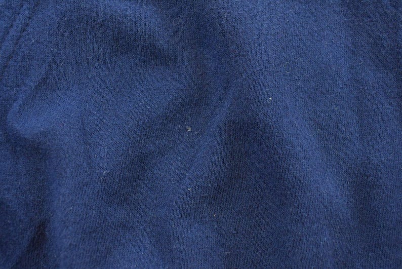 K&ouml;nnte beinhalten: Nahaufnahme eines strukturierten, marineblauen Stoffes. Das Material scheint ein Strick- oder Webtextil zu sein, mit subtilen Farb- und Texturvariationen. Der Stoff hat ein leicht abgenutztes Aussehen.