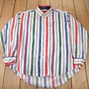 May include: A long-sleeved button-down shirt with a white background and multicolored vertical stripes. The stripes are red, blue, green, purple, and gray.