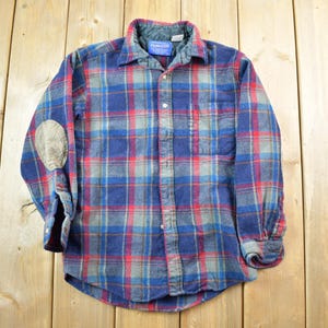 May include: A blue, red, and gray plaid flannel shirt with elbow patches. The shirt has a button-down front, a collar, and a chest pocket. The shirt is made of a soft, warm material, perfect for cooler weather.