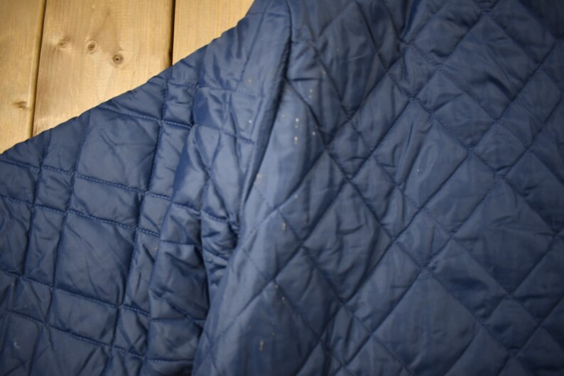 May include: A navy blue quilted jacket with a diamond pattern. The jacket is made of a soft, comfortable material and has a relaxed fit.