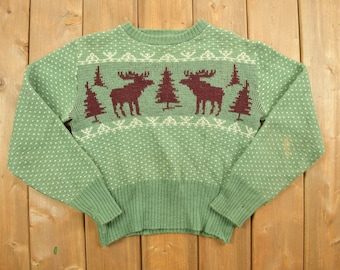 May include: A green knitted sweater with a white and brown moose pattern. The sweater has a crew neck and long sleeves.