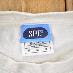 May include: A white t-shirt with a blue tag that says "SPL28" and "HECHO EN MEXICO FABRICADO EN MEXICO MADE IN MEXICO" with the size "M" printed three times.