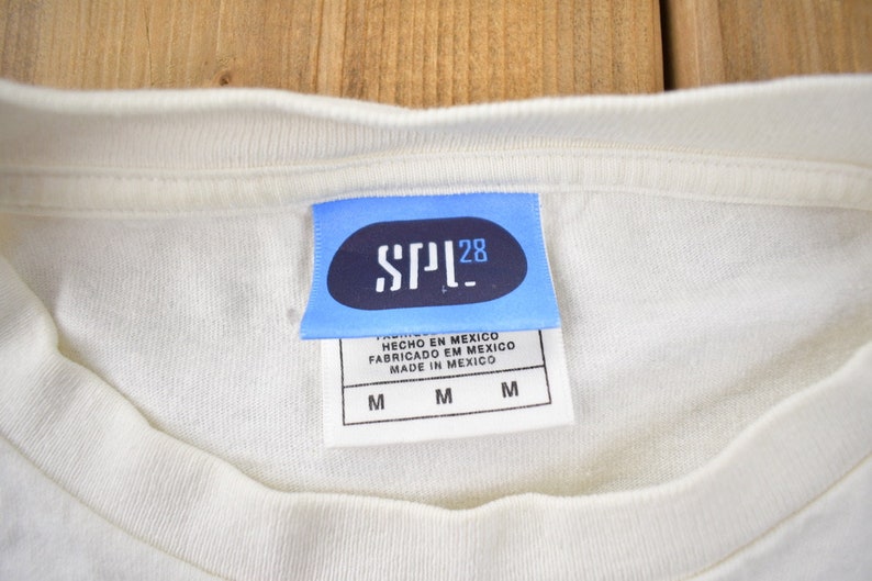 May include: A white t-shirt with a blue tag that says "SPL28" and "HECHO EN MEXICO FABRICADO EN MEXICO MADE IN MEXICO" with the size "M" printed three times.