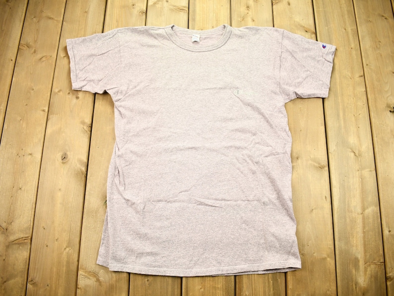 May include: A heather grey t-shirt with a small logo on the left chest and a larger logo on the right sleeve.