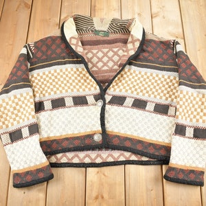 May include: A brown, black, and white patterned cardigan with a shawl collar and a button closure. The cardigan has a cropped length.