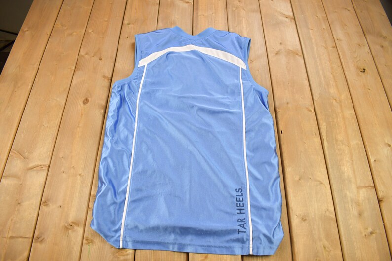 May include: A light blue sleeveless shirt with white trim and the text "TAR HEELS" on the back.