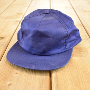 Könnte beinhalten: Vintage marineblaue Baseballkappe mit gebogenem Schirm. Die Kappe besteht aus strapazierfähigem Stoff und hat ein klassisches sechsteiliges Design. Der Hut ist einfarbig und hat einen Knopf oben.