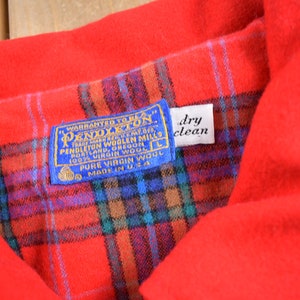 Pu&ograve; includere: Una camicia Pendleton a quadri rossi con un'etichetta blu che recita "Warranted to be a Pendleton" e "100% Virgin Wool". L'etichetta include anche le parole "Pendleton Woolen Mills" e "Made in U.S.A.". Un'etichetta bianca con le parole "dry clean" &egrave; attaccata all'etichetta.