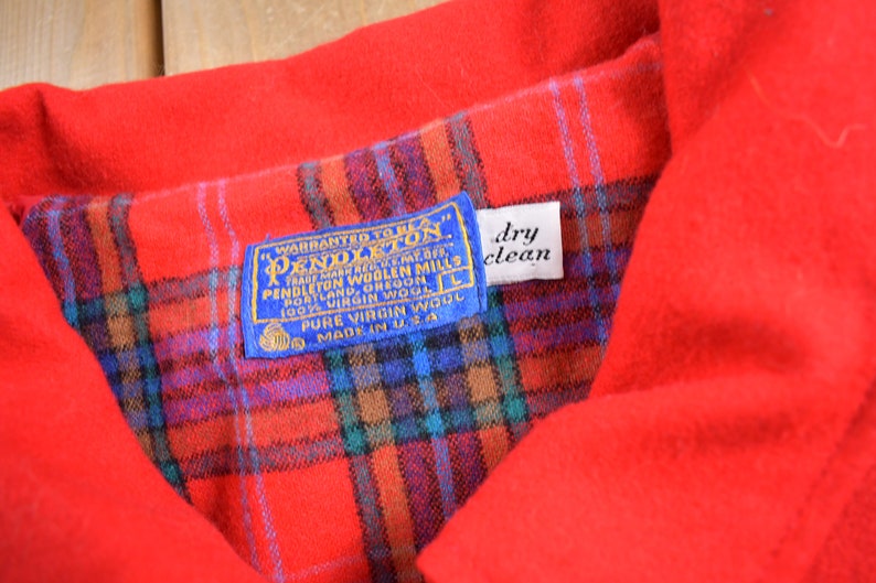 Pu&ograve; includere: Una camicia Pendleton a quadri rossi con un'etichetta blu che recita "Warranted to be a Pendleton" e "100% Virgin Wool". L'etichetta include anche le parole "Pendleton Woolen Mills" e "Made in U.S.A.". Un'etichetta bianca con le parole "dry clean" &egrave; attaccata all'etichetta.