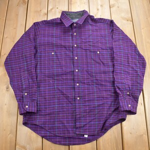 May include: A long-sleeved plaid shirt in shades of purple, green, and black. The shirt has a button-down collar and a button-up front.