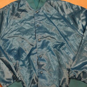May include: Teal satin jacket with a button-up front and green ribbed cuffs and collar. The jacket has a shiny, smooth texture and a relaxed fit. The jacket is a vintage style.