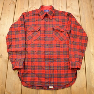 May include: A red and blue plaid flannel shirt with a button-down collar and two chest pockets.
