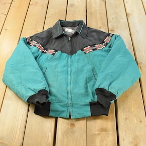 May include: A teal and black zip-up jacket featuring a pointed collar, long sleeves with black ribbed cuffs, and a black ribbed hem. The upper chest and shoulder area are black, accented by a horizontal band with a geometric pattern in red, white, and teal.