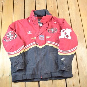 Könnte beinhalten: Rote, schwarze und goldfarbene Vintage-Jacke mit dem Logo der San Francisco 49ers auf den Ärmeln und der Brust. Die Jacke hat das NFL-Logo und weiße Sterne auf dem rechten Ärmel. Sie hat einen Reißverschluss und einen hohen Kragen.