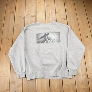 May include: Gray sweatshirt with a black and white image of Eeyore the donkey from Winnie the Pooh. The image shows Eeyore looking up at a yellow butterfly with the text "Feel Your Dreams" and "The Magic of Dreams" below the image.
