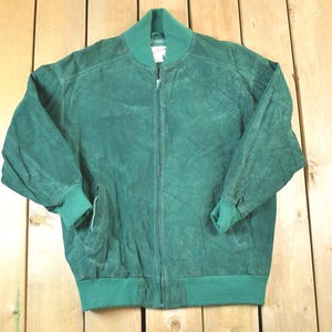 Peut inclure: Veste de bombardier en daim vert avec fermeture éclair complète. La veste a un col, des poignets et un ourlet côtelés. La veste est de couleur unie et de style vintage classique.
