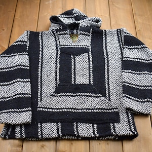 May include: Black and white striped hooded poncho with a pocket on the front. The poncho is made of a soft, woven fabric.