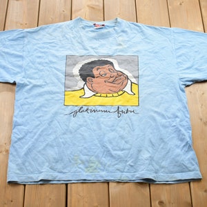 May include: A light blue t-shirt featuring a cartoon image of a man wearing a yellow shirt, with the text "platinum future" printed on the front.