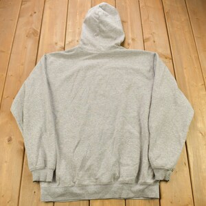 Puede incluir: Una sudadera gris con capucha y cord&oacute;n de ajuste. La sudadera tiene mangas largas y un bolsillo canguro.