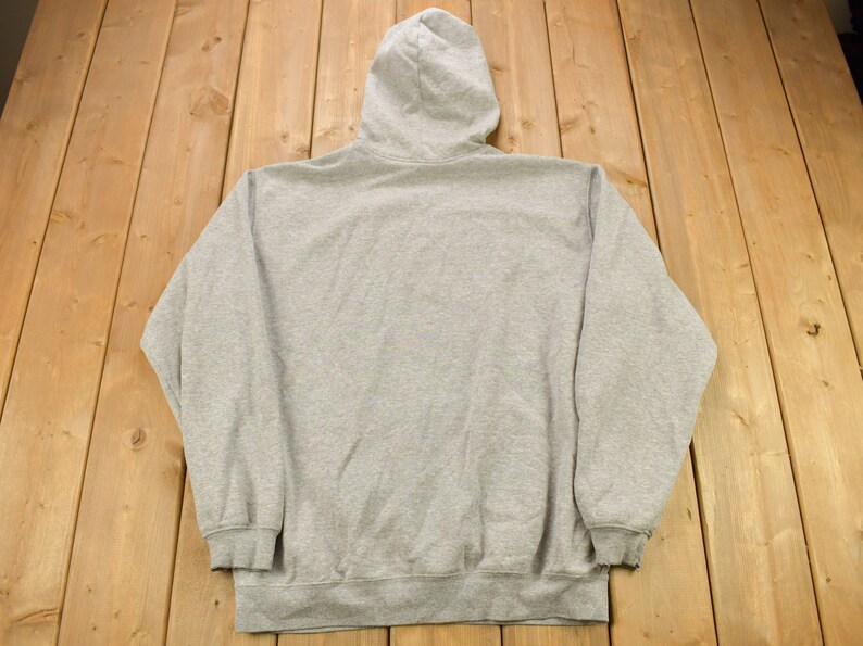 Puede incluir: Una sudadera gris con capucha y cord&oacute;n de ajuste. La sudadera tiene mangas largas y un bolsillo canguro.