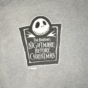 Puede incluir: Camiseta gris con un dise&ntilde;o gr&aacute;fico en blanco y negro de Jack Skellington de "Pesadilla antes de Navidad" de Tim Burton. El dise&ntilde;o incluye el t&iacute;tulo de la pel&iacute;cula. El logotipo de Disney est&aacute; en la parte inferior.