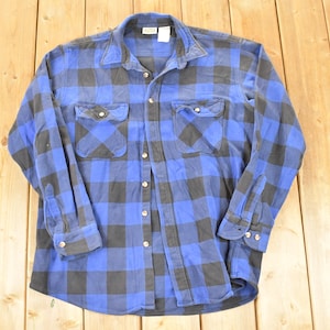 May include: A blue and black checked button-down shirt with two chest pockets. The long-sleeved shirt has a collared neckline and buttoned cuffs. The shirt is made of a soft, possibly flannel, material.