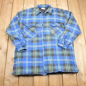 Puede incluir: Una camisa de franela a cuadros azules, verdes y blancos con cierre de botones y dos bolsillos en el pecho.