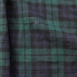 Puede incluir: Primer plano de una secci&oacute;n de tela con un patr&oacute;n de cuadros cl&aacute;sico. El dise&ntilde;o presenta una cuadr&iacute;cula de l&iacute;neas que se cruzan en tonos de verde y azul marino. La tela tiene un aspecto ligeramente texturizado.